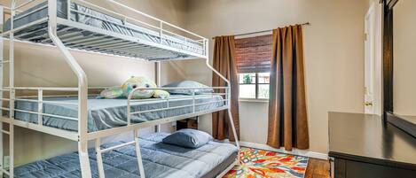 A bunk bed room with a ceiling fan, a window with curtains, and a colorful rug.