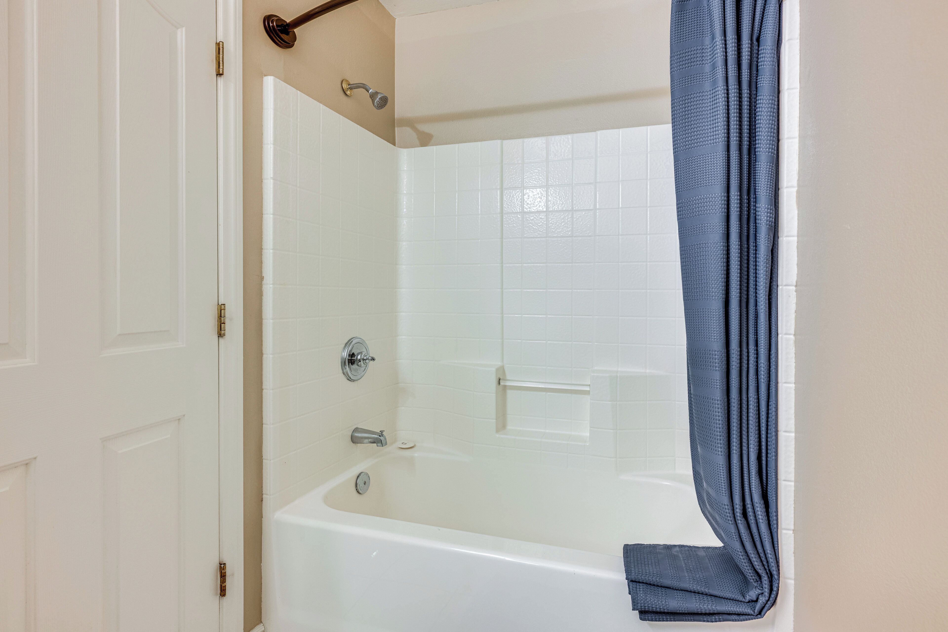 A bathroom with a white bathtub, a shower, and a towel hanging on the wall.