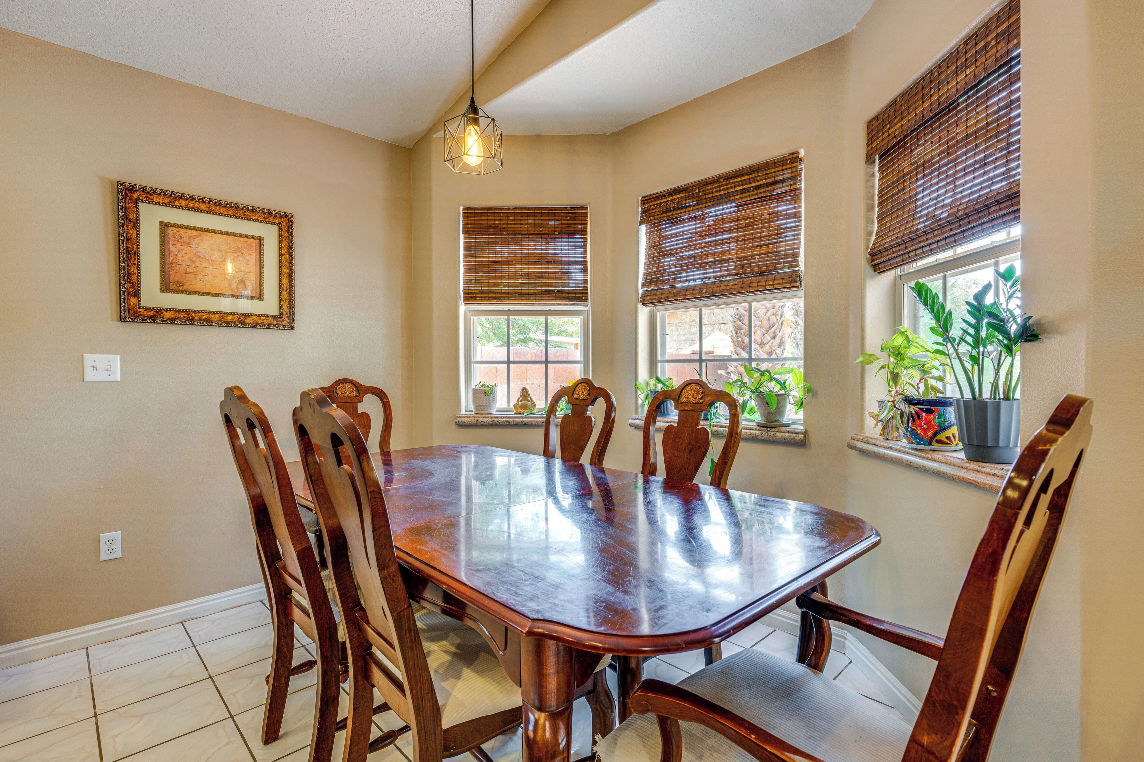 A dining area with a wooden table and chairs, a hanging light fixture, and windows with blinds.