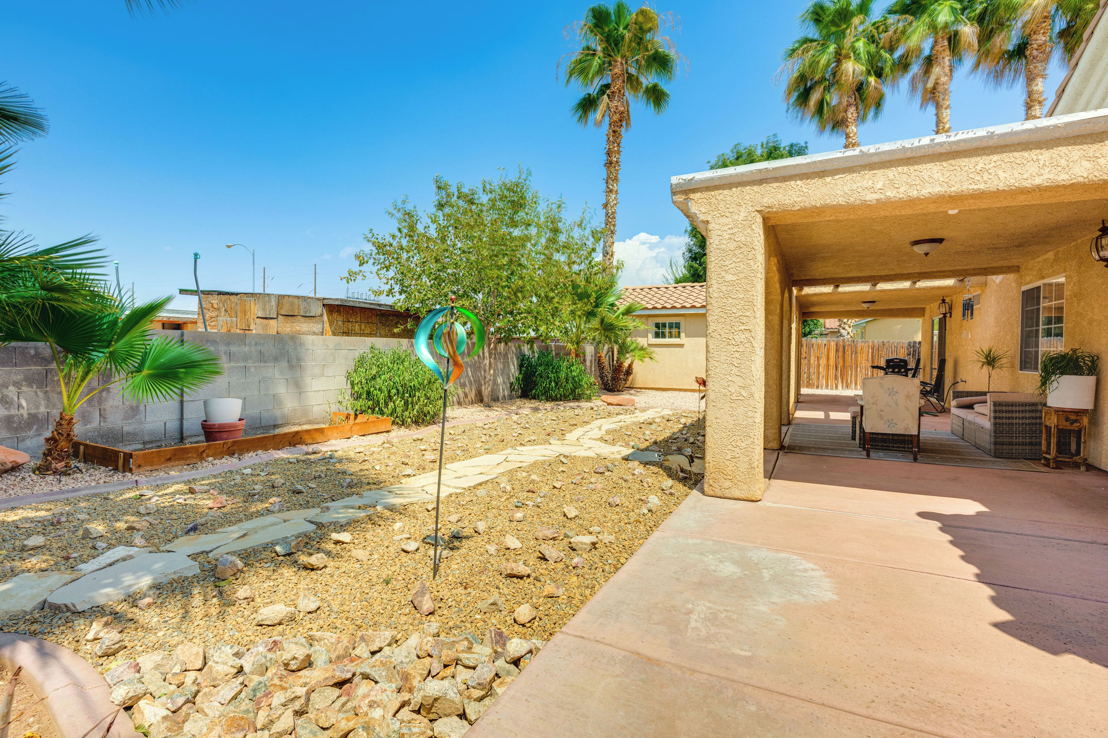 A patio area with a stone pathway, palm trees, and a covered seating area with a table and chairs.