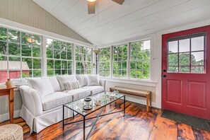 A cozy room with a white sofa, a glass coffee table, and a red door. - Historic Farmhouse Near Mountains & Colleges! (Westfield)