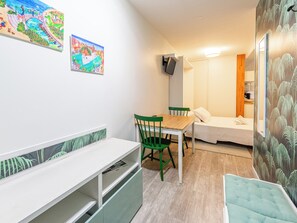 A small, cozy room with a wooden table and chairs, a bed with a white mattress, and a wall-mounted TV. - Lachenal - Studio proche du centre historique (Annecy)