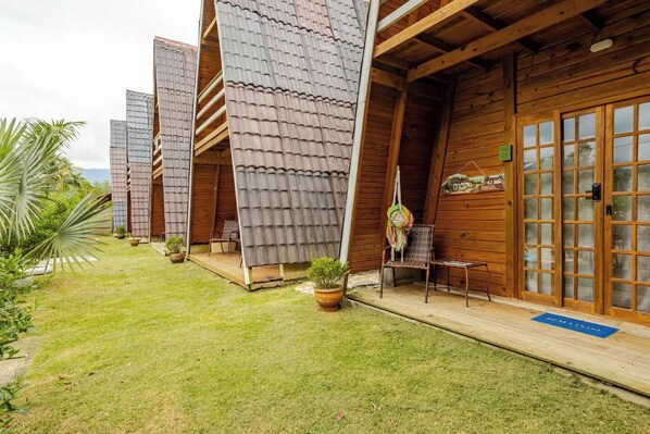A row of wooden cabins with sloped roofs, each with a small porch and a chair. - Chales DuCarmo (Angra dos Reis)