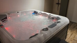 Un bain à remous doté de jets d’eau et de lumières rouges, d’une pomme de douche et d’un panneau de commande.