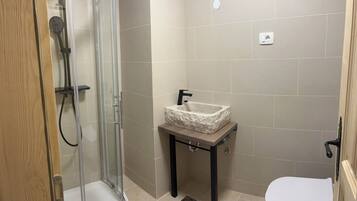 A small bathroom with a glass shower enclosure, a sink with a marble-like countertop, and a toilet.