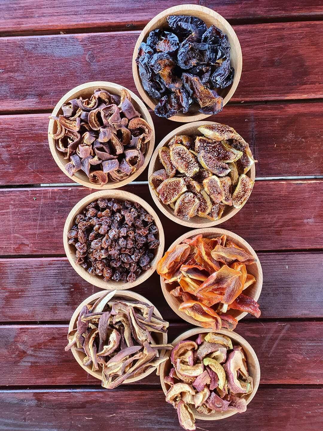 Seven wooden bowls containing various dried fruits and vegetables arranged on a wooden surface.