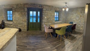 Une pièce rustique aux murs de pierre, avec une table à manger en bois et des chaises colorées.
