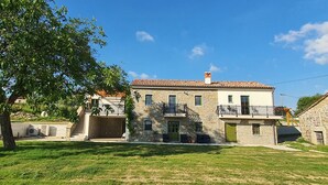 Une maison en pierre à deux étages, avec un toit recouvert de tuiles, un balcon et un petit jardin.