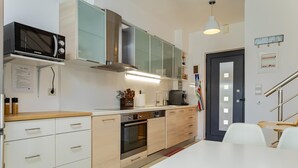 A modern kitchen with a microwave, oven, and coffee maker. There is a white table and chairs, and a door with a handle. - The Base- Homey, Affordable, in Good Location (Apokoronas)