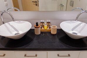 Un baño con dos lavamanos blancos, una encimera negra y una bandeja de madera con artículos de aseo.