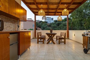 Un patio con una mesa y sillas de madera, una cocina integrada con armarios e iluminación colgante.