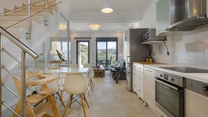 A modern kitchen with stainless steel appliances, a dining area with wooden chairs, and a staircase with metal railings. - The Base- Homey, Affordable, in Good Location (Apokoronas)