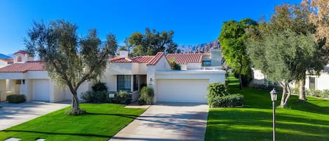 A row of single-family homes with red-tiled roofs, a well-maintained lawn, and a clear blue sky.