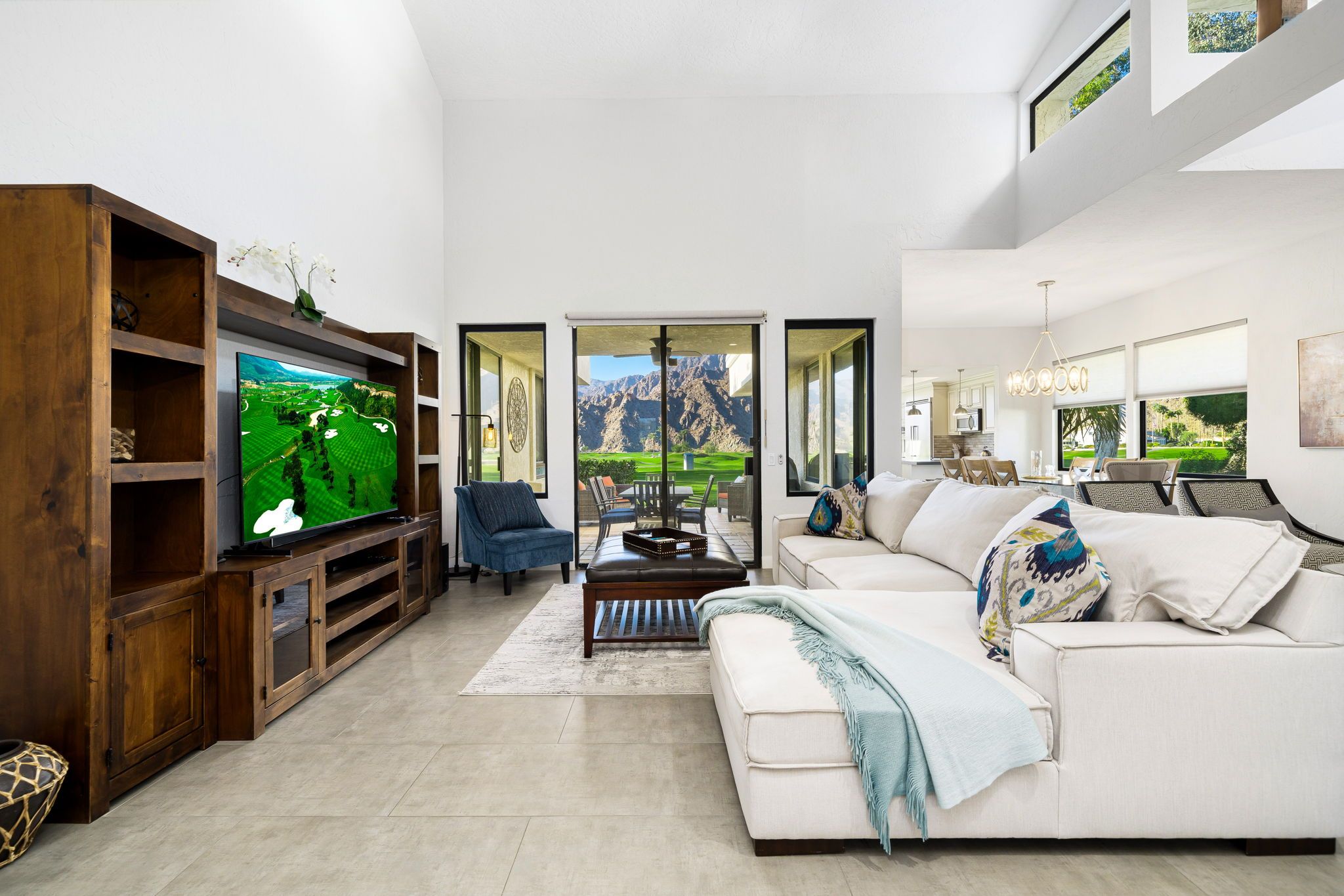 A modern living room with a large flat-screen TV, a white sofa, a blue armchair, and a wooden entertainment unit.
