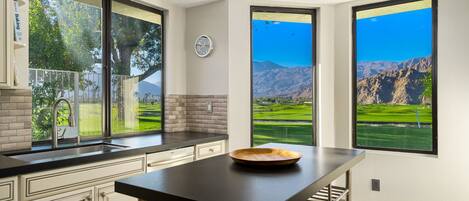 A kitchen with a large window, a clock, and a bowl on the counter.