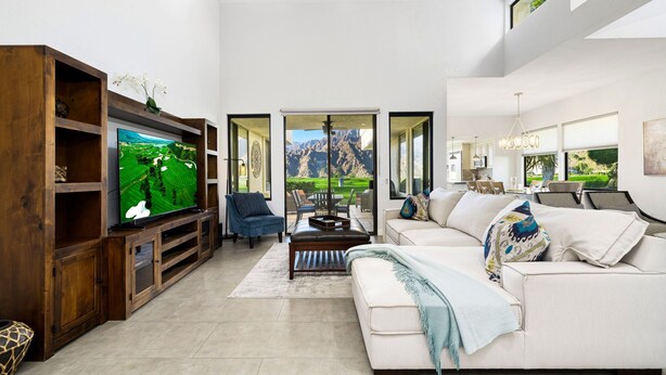 Un salon moderne doté d’un grand téléviseur à écran plat, d’un canapé blanc, d’un fauteuil bleu et d’un meuble de rangement en bois.