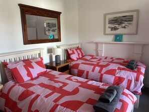 Une chambre avec deux lits, chacun agrémenté de draps rouges et blancs, une table de chevet avec une lampe, un miroir et un tableau encadré au mur.