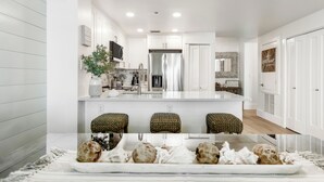 Une cuisine moderne avec des meubles blancs, un îlot central et un coin repas agrémenté d’une nappe blanche et d’objets décoratifs.
