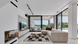 A modern living room with a sectional sofa, a flat-screen TV, a fireplace, and a large window offering a view of the outdoors. - NEW Luxury villa I infinity pool (Starigrad)