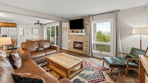A living room with a fireplace, leather sofa, wooden coffee table, and a view of greenery through large windows. - Best Views in the Valley~Near Skiing~Winter Shuttle (Steamboat Springs)