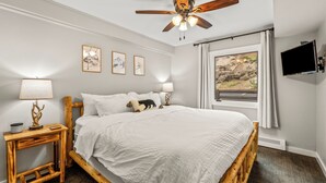 A bedroom with a wooden bed, ceiling fan, bedside lamps, framed pictures, and a TV. - Best Views in the Valley~Near Skiing~Winter Shuttle (Steamboat Springs)