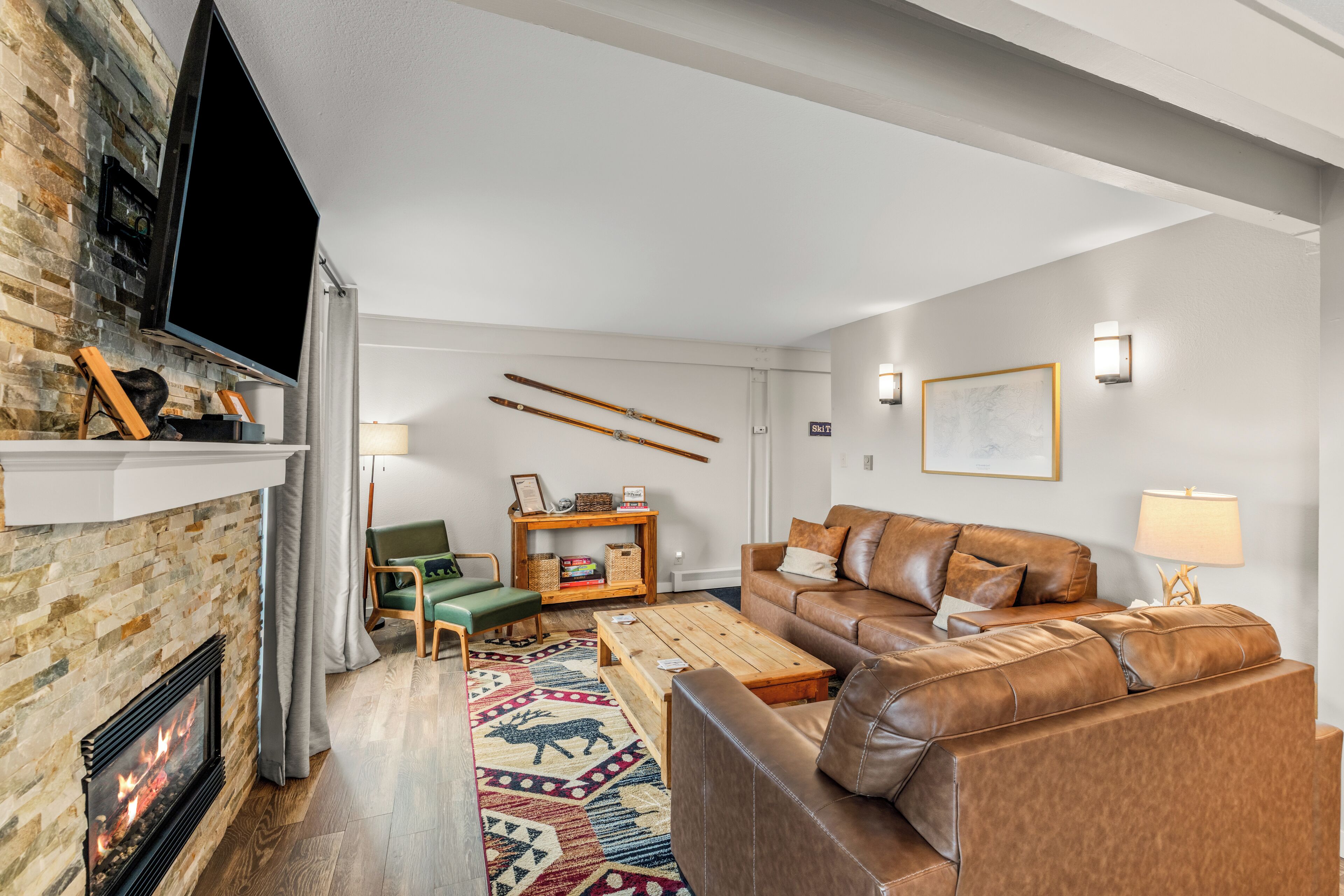 Una sala de estar con chimenea, sofá de cuero, mesa de centro de madera y esquíes en la pared.