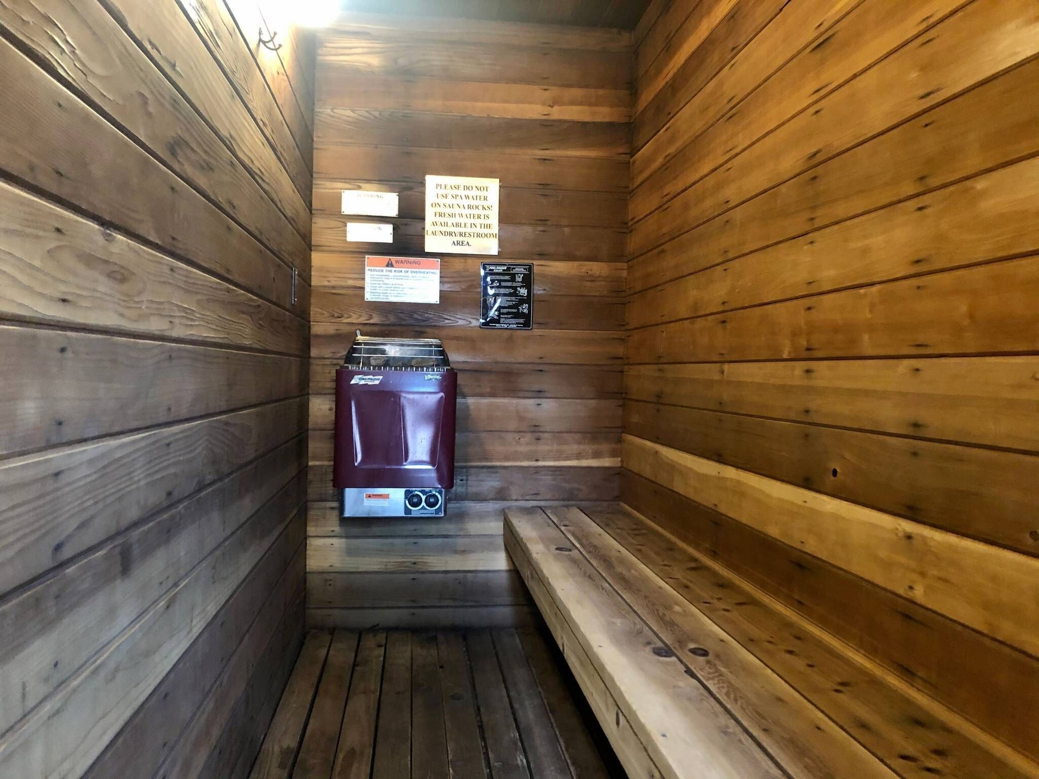 A sauna room with wooden walls, a bench, and a water heater. There are signs with instructions and warnings.