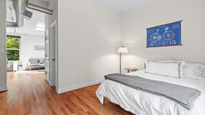 Een slaapkamer met een bed, een nachtkastje, een lamp en een blauw kunstwerk aan de muur.