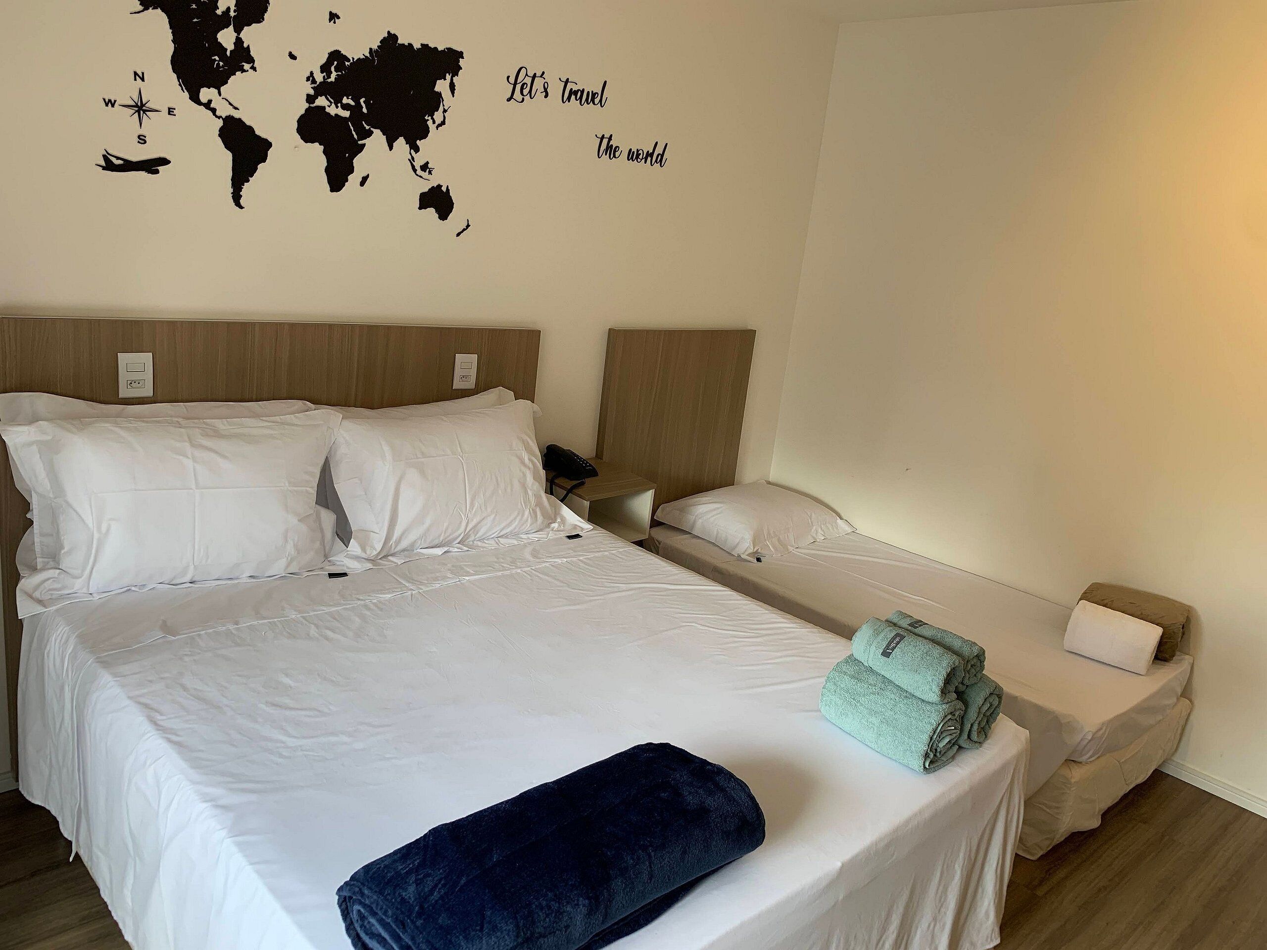 Une chambre d’hôtel avec deux lits, une carte du monde accrochée au mur et une pancarte sur laquelle on peut lire : « Partons à la découverte du monde ».