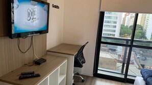 Hotellihuone, jossa on seinälle asennettu televisio, työpöytä tuolilla sekä suuri ikkuna, josta avautuu näkymä kaupunkiin.