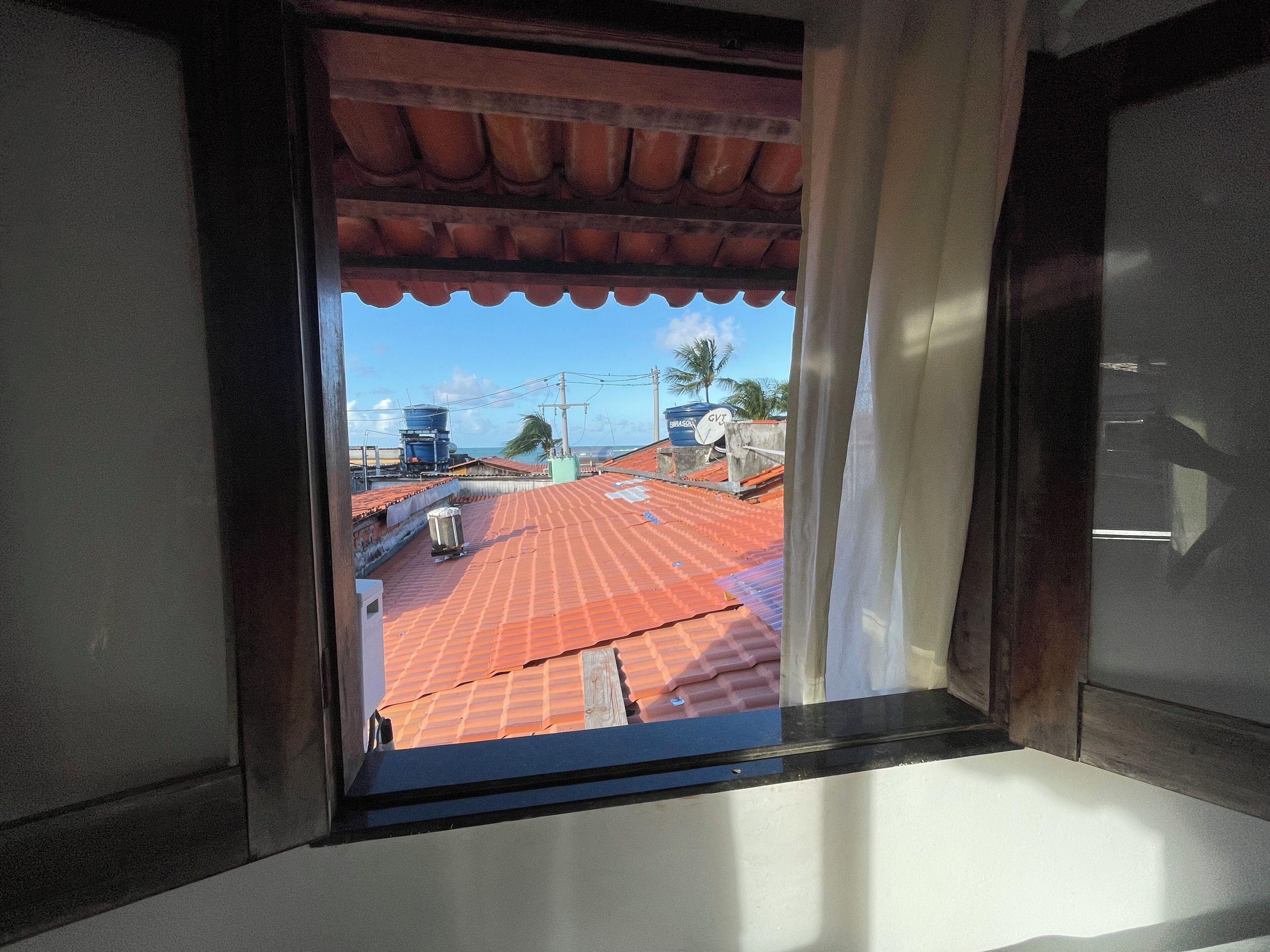 Vista pela janela de um telhado vermelho com cortina branca entreaberta.