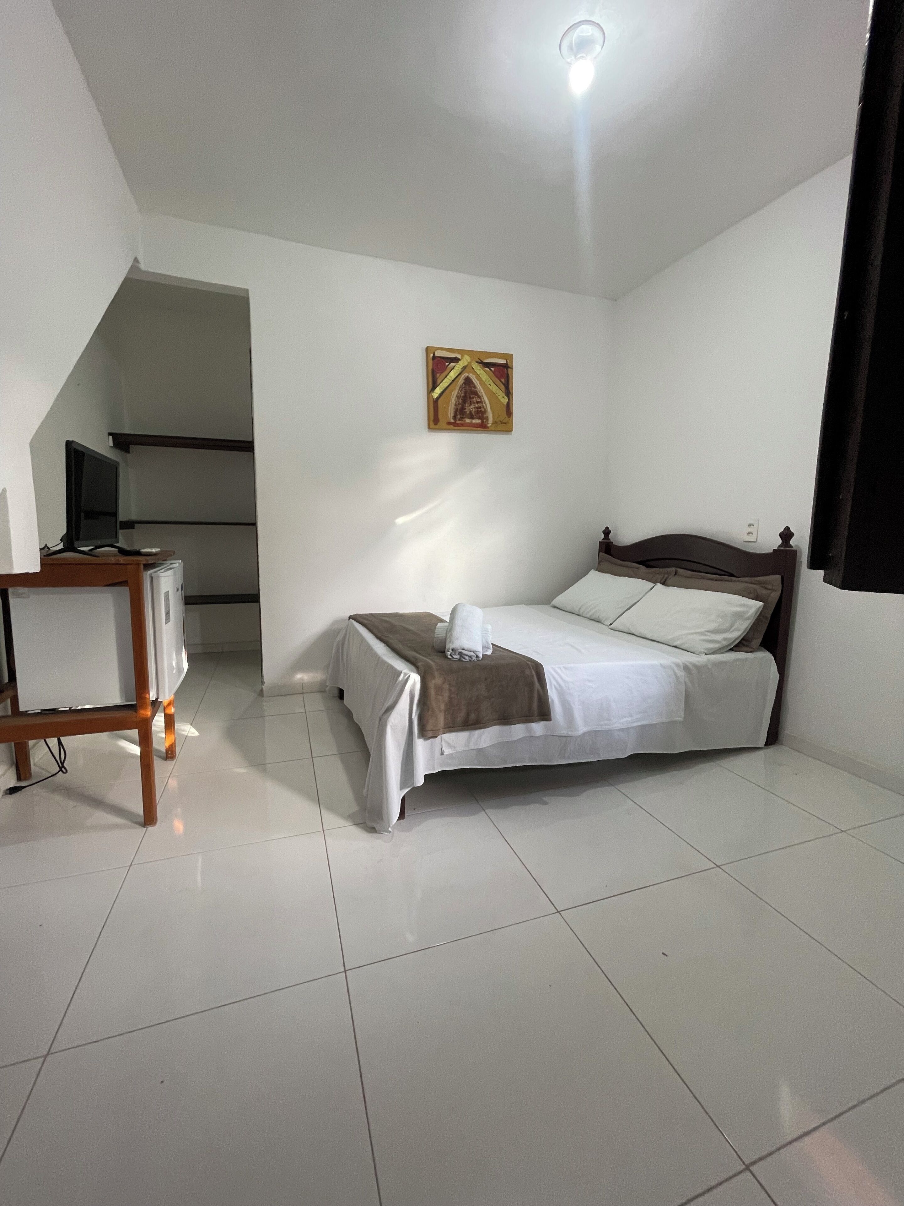 A bedroom with a bed, a desk, and a ceiling light.