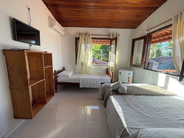 A room with two beds, a TV, an air conditioner, and a window with curtains. - Pousada Vila Nova (Cairu)