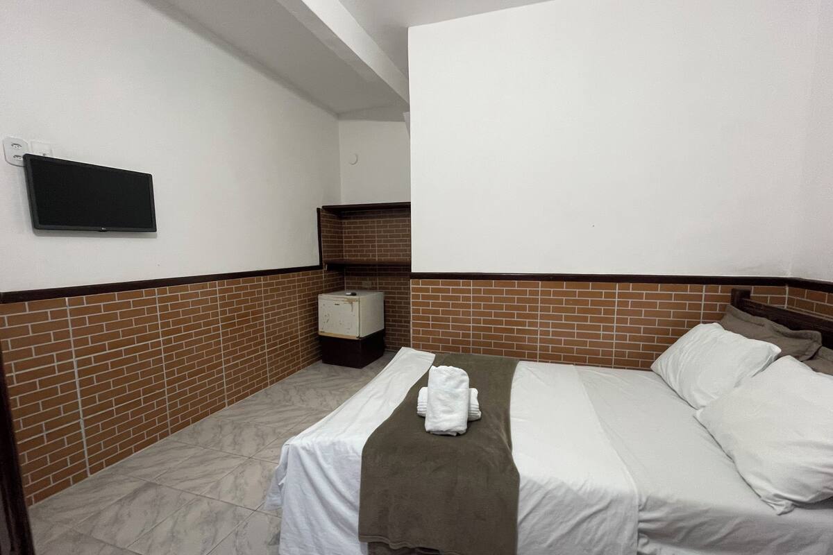 A small, clean room with a bed, a TV, and a small cabinet.