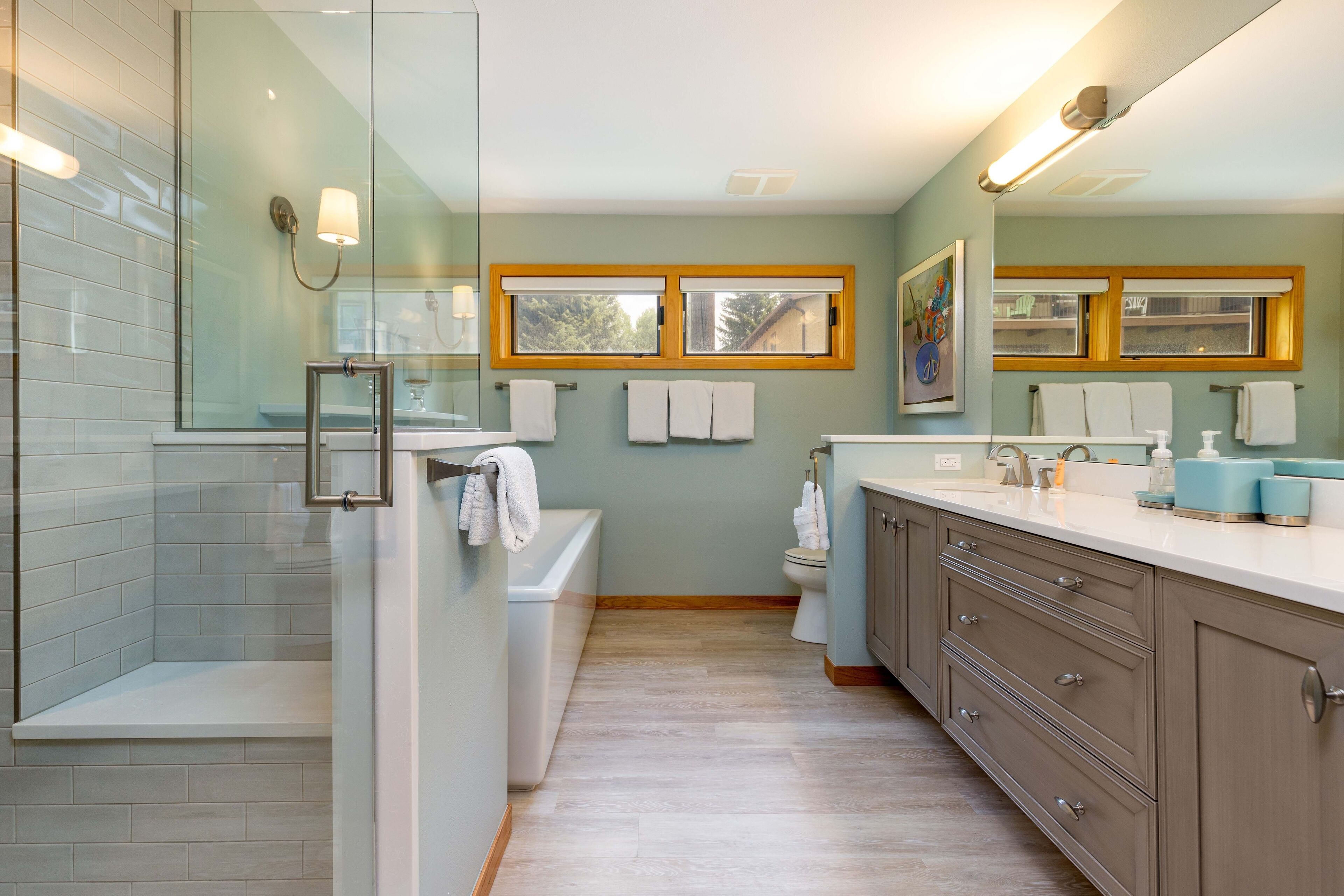 A modern bathroom with a glass shower enclosure, a bathtub, a toilet, and a vanity with drawers and a mirror.