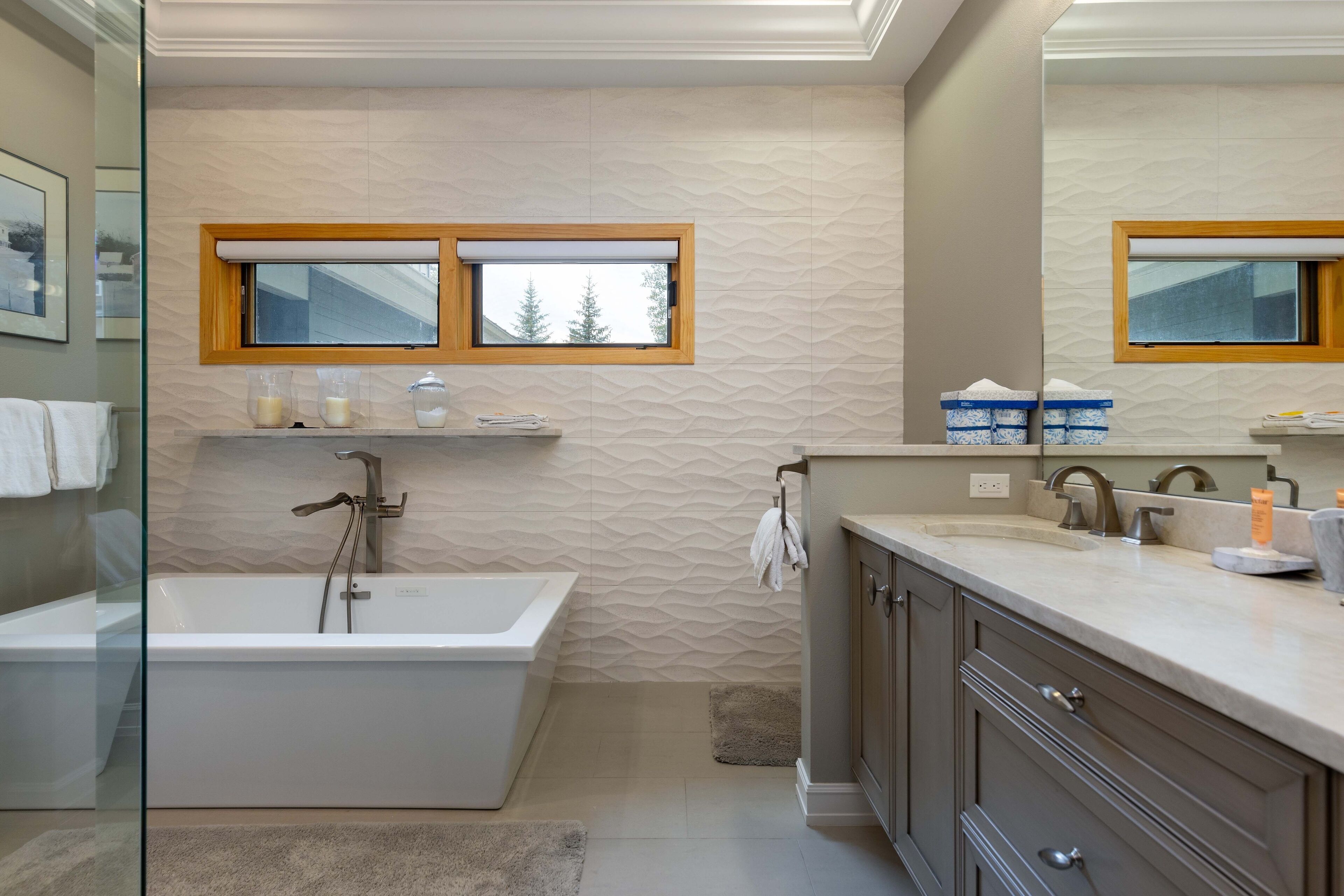 A modern bathroom with a freestanding bathtub, a vanity with a mirror, and a window above the sink.