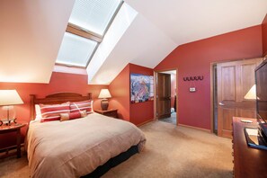 A bedroom with a skylight, a bed with multiple pillows, a nightstand with a lamp, a wooden wardrobe, and a door leading to another room. - Select Unit 1710 - 2br - Zephyr Mountain Lodge 2 Bedroom Condo (Winter Park)