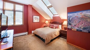 Ein Schlafzimmer mit Bett, Schreibtisch, Lampe, einer Karte an der Wand und Dachfenstern.