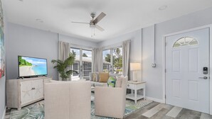 A living room with a sofa, armchair, TV, and a ceiling fan. - Dune Our Thing - Building A - 171 Washington 3 Bedroom Condo by RedAwning (Fort Myers Beach)