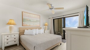 Un dormitorio con cama, mesitas de noche, ventilador de techo, un cuadro y vistas a través de una ventana.