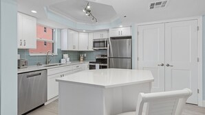 A modern kitchen with white cabinetry, stainless steel appliances, and a central island. - Beach Villas # 306 by RedAwning - 15% off through September 2024 (Fort Myers Beach)