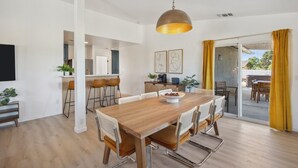 Un vaste espace dédié à la salle à manger, avec une table en bois et des chaises modernes, une cuisine à l’arrière-plan et une porte-fenêtre coulissante donnant sur une terrasse extérieure.
