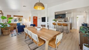 Une cuisine moderne équipée d’appareils électroménagers en acier inoxydable, un coin repas avec une table et des chaises en bois, et un salon avec un canapé et un téléviseur.