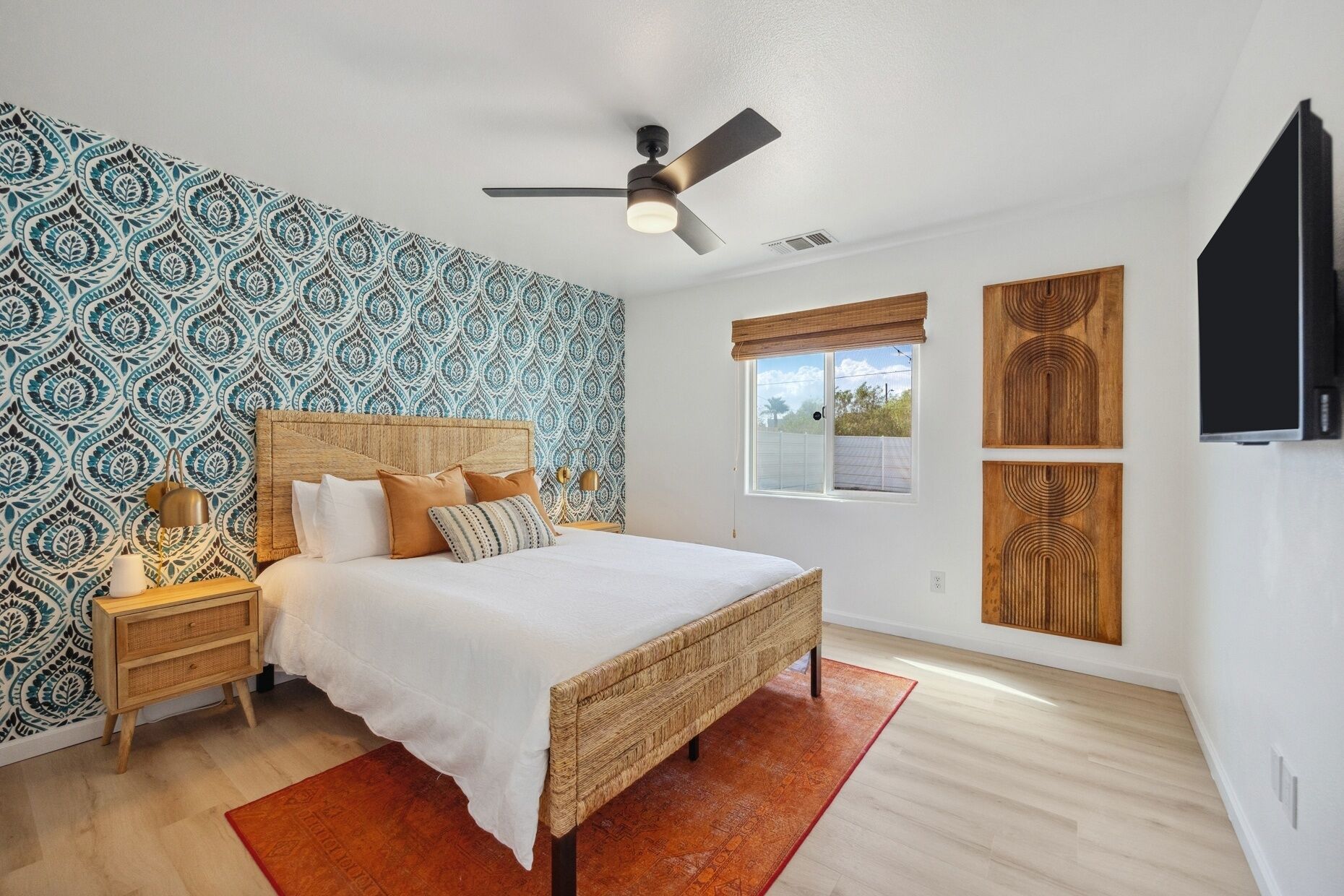 A bedroom with a patterned wallpaper, a wooden headboard, a bed with white bedding, a nightstand, a floor lamp, and a ceiling fan.