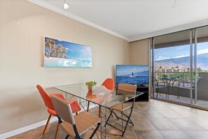 Ein modernes Wohnzimmer mit Glastisch, Korbstühlen, einem Flachbildfernseher und einem großen Fenster mit Balkon und schöner Aussicht.