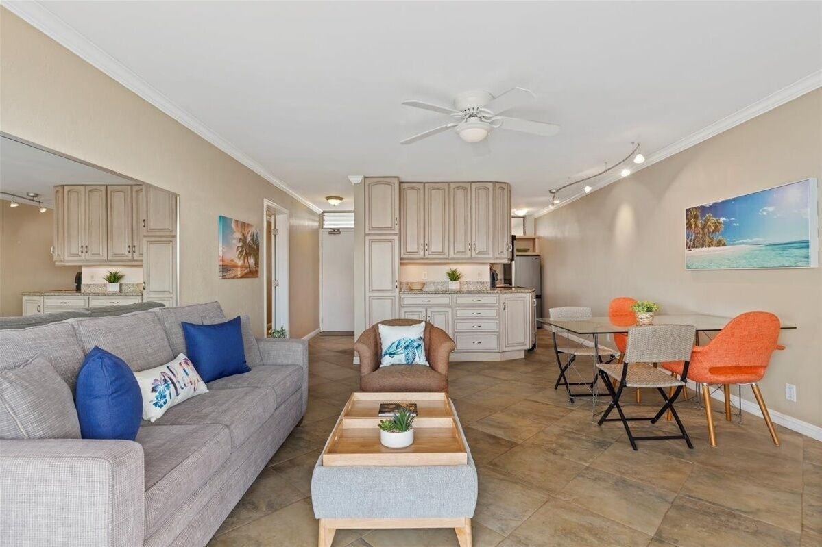 A modern living room with a grey sofa, a brown armchair, and a dining area with orange chairs.