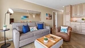 A living room with a grey sofa, a brown armchair, a wooden coffee table, a floor lamp, and a ceiling fan. - Nani Kai Hale 604 1 Bedroom Condo (Kihei)