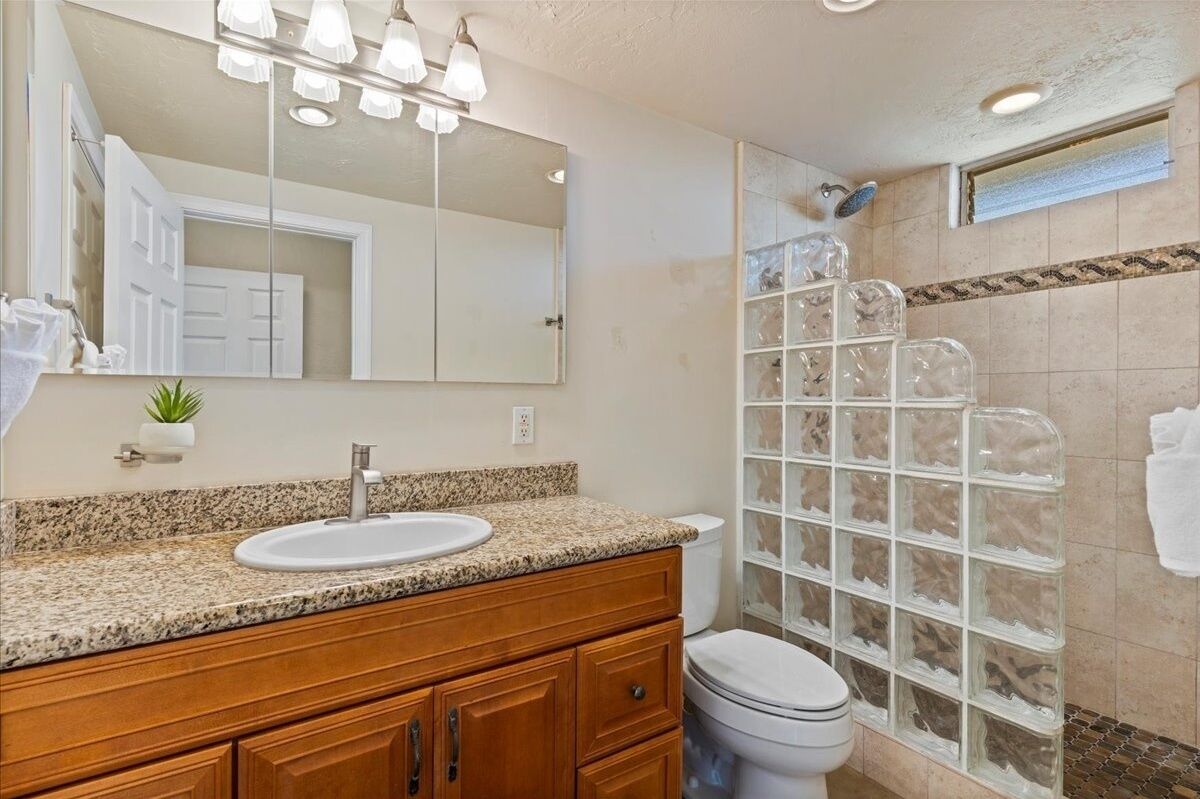 A bathroom with a granite countertop sink, wooden vanity, a large mirror, and a glass shower enclosure.