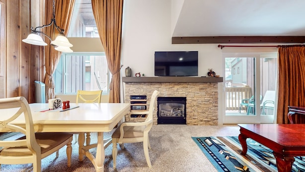 A cozy living room with a stone fireplace, a flat-screen TV mounted above it, and a dining area with a table and chairs.