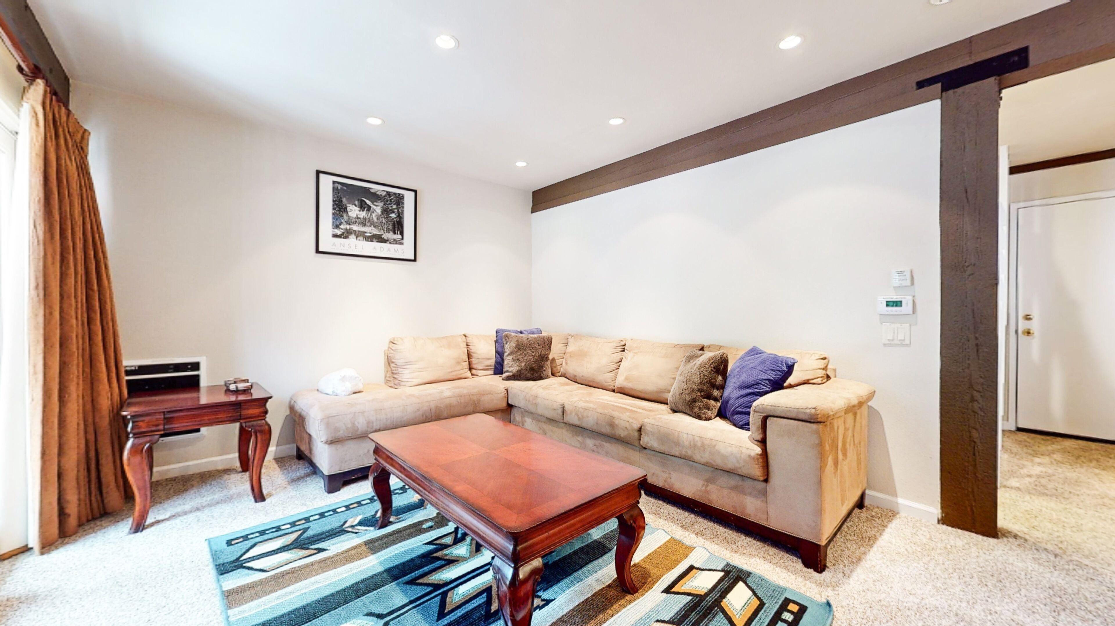 Un salon avec un canapé d’angle beige, une table basse en bois et des tapis à motifs.
